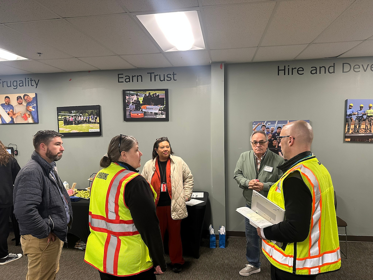 A man and woman in reflective vests talk to two men and a woman.