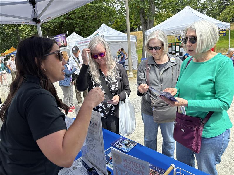 One young woman speaks to three older women in sunglasses at a booth.