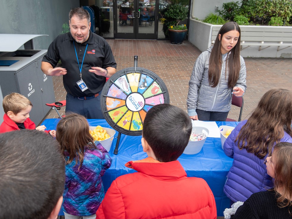 Port employees stand behind a table with a prize wheel while talking to the public.
