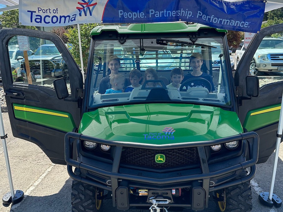 A group of children smile while sitting in the cab of a John Deere tractor. 