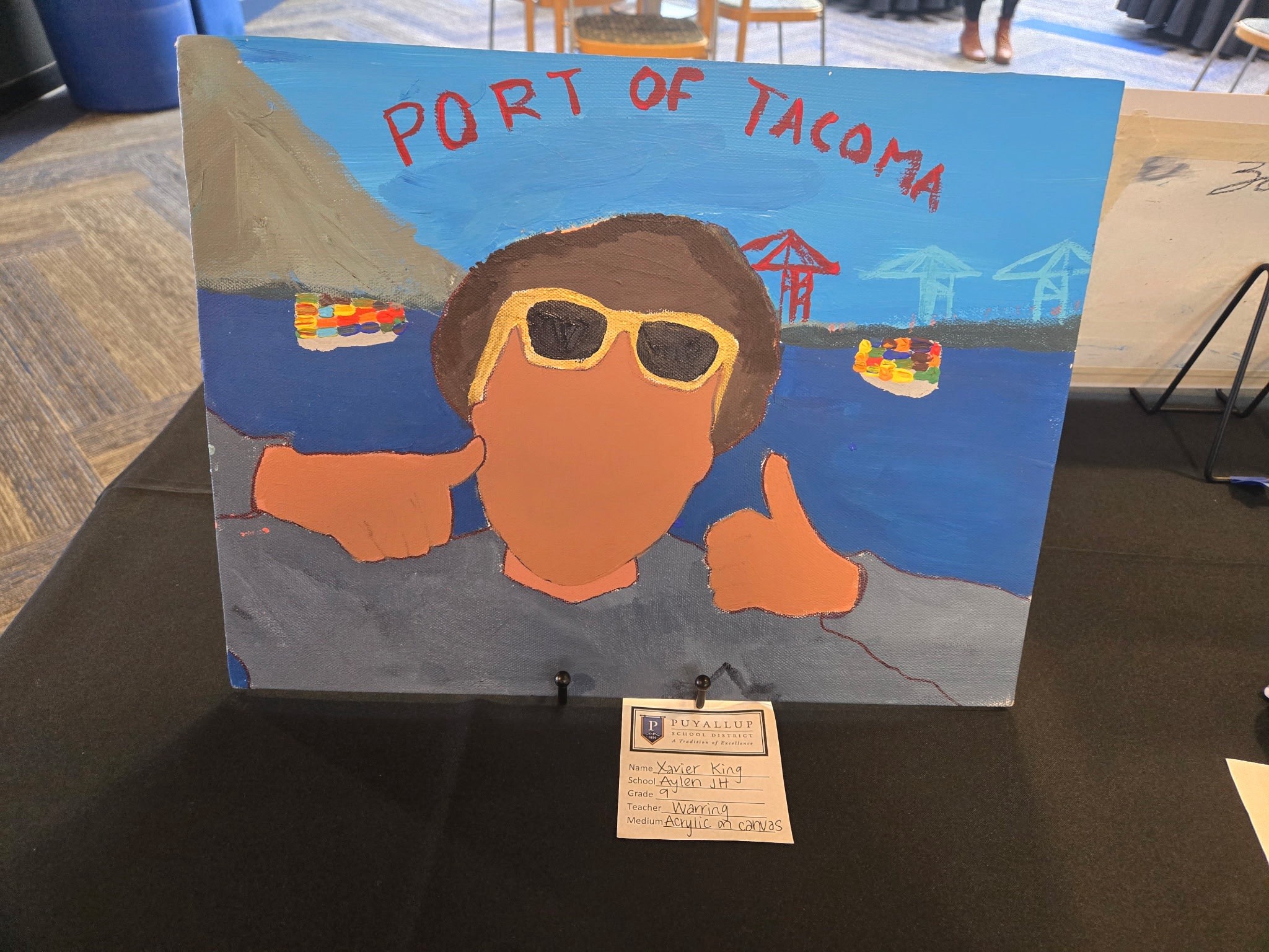 Student-created painting of a young man in sunglasses holding two thumbs up with 'Port of Tacoma' written behind him.