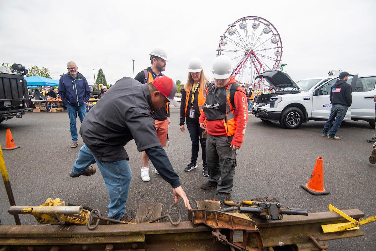 Students in protective gear looking at a technician explaining the parts of a rail track.