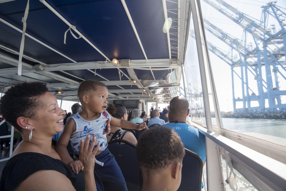 A woman holding a toddler up to look off the deck of a boat.
