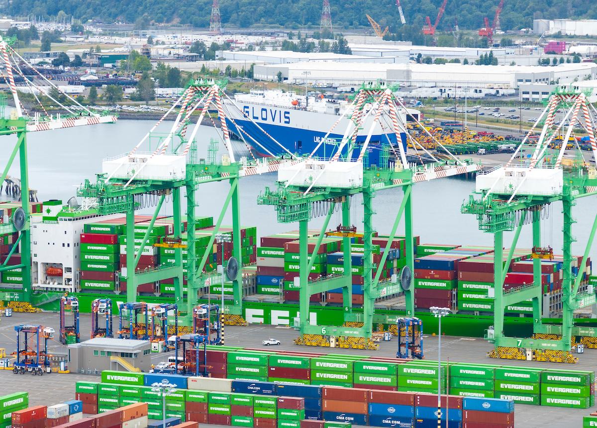 Drone shot of cargo operations and container ships at a Port with a ship in the background. 