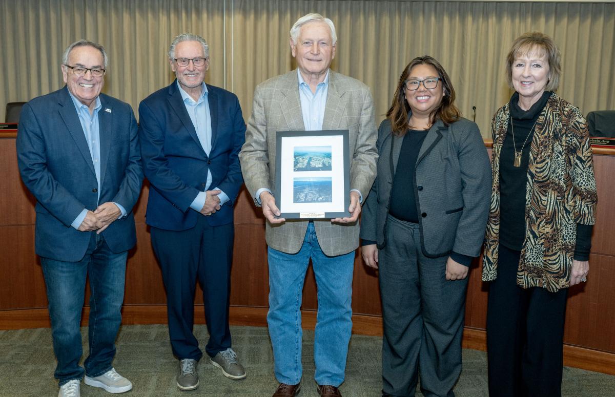 Three men and two women standing together while one man holds a matted photo. 