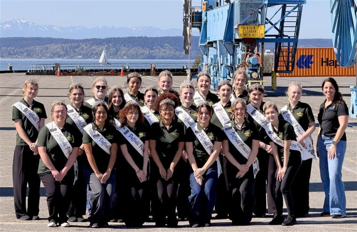 A group of Daffodil Festival princesses post on a port terminal with an employee.