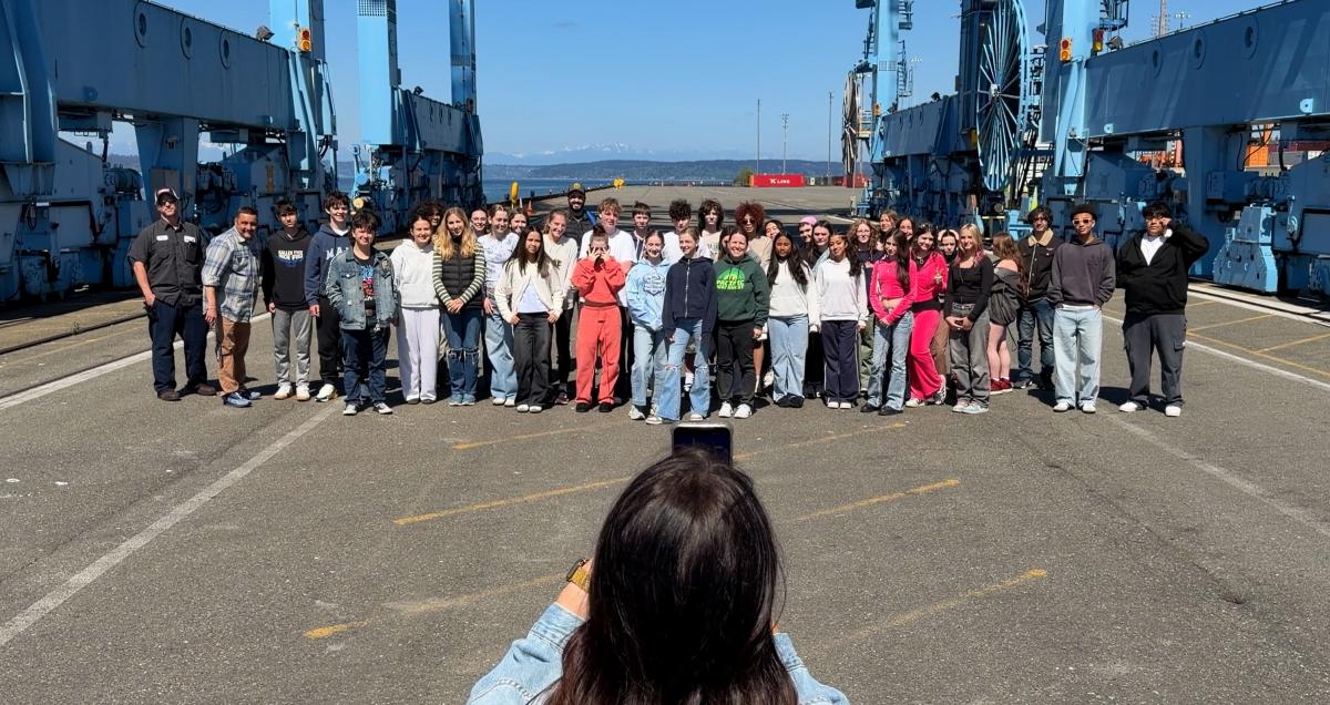 A Port employee takes a photo of a group of students on a Port terminal.