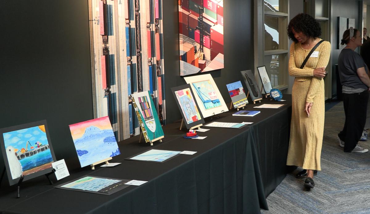 A woman looks at student art pieces on tables in the Port administration building atrium.