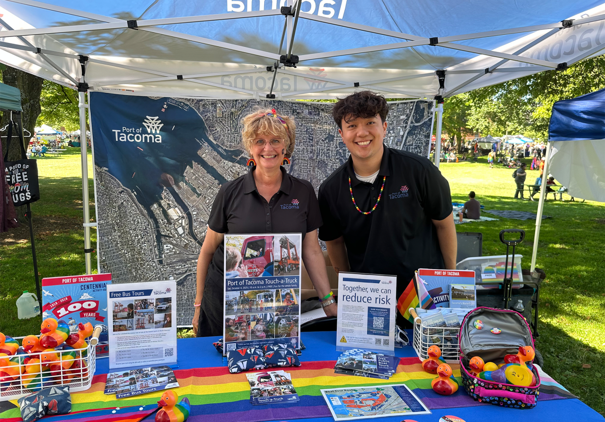 A man and woman stand smiling at a pride booth.