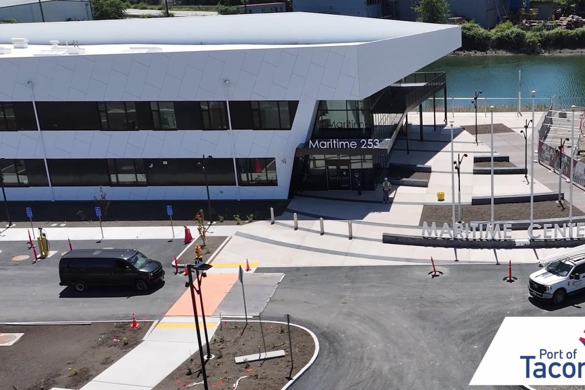 A modern white building and parking lot with two vehicles in front.